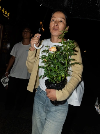一位女子手里拿着一株植物 站在雨中 手里还拿着一把伞。