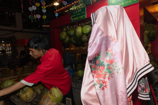 一位穿粉色衣服的女士在一个市场的小店正在切新鲜椰子。