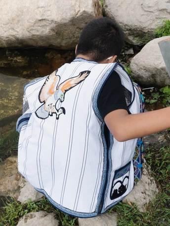 一个背着书包的年轻男孩正在伸出手去摸一条流动在岩石下方的溪流中的小动物。