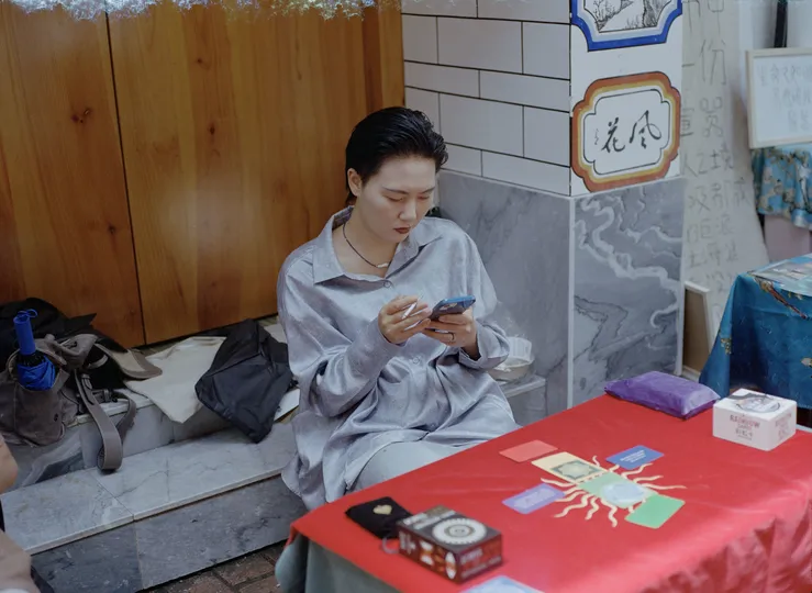 一位女性坐在红色的桌子旁 一只狗正在注视她的手机。