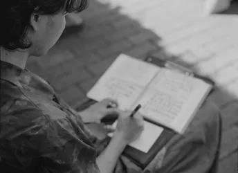 一位年轻女孩坐在长凳上 正在笔记本上写笔记 而一位年轻男孩正在阅读一本书。