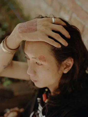 一位面部有纹身、头发上有纹身的年轻女子 将手放在额头前。