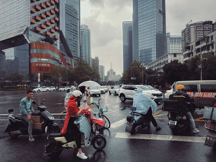 一些人骑着滑板车和摩托车穿过雨中的城市街道。