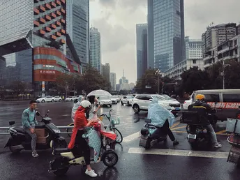 一些人骑着滑板车和摩托车穿过雨中的城市街道。