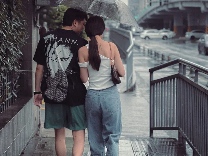 一位年轻男子和一位年轻女子站在雨中人行道上 在伞下。