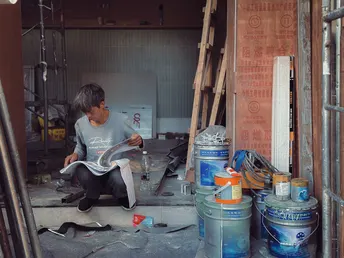 一个男子坐在车库地板上阅读报纸 一个年轻男孩阅读杂志。