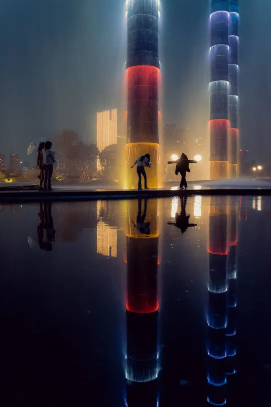 夜晚的城市 人们站在水中 雾中一高塔被点亮。
