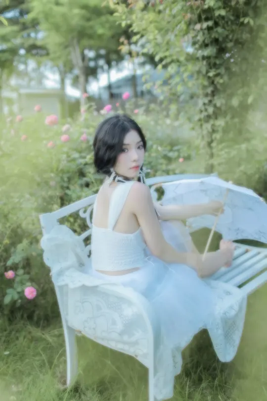 一个穿着白色连衣裙的年轻女子坐在花园里的蓝色长凳上