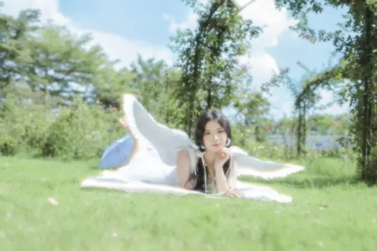 一个年轻女子躺在公园的白毛毯上 周围是绿草和树木。