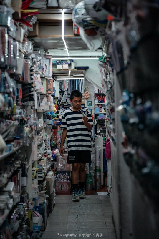 一个狭窄的商店过道 一个年轻人走在通道上 有人站在门口。