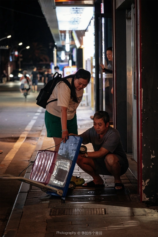 一个人在人行道上 夜晚 跪在地上 旁边站着一个行李 旁边站着一个站立的女人。