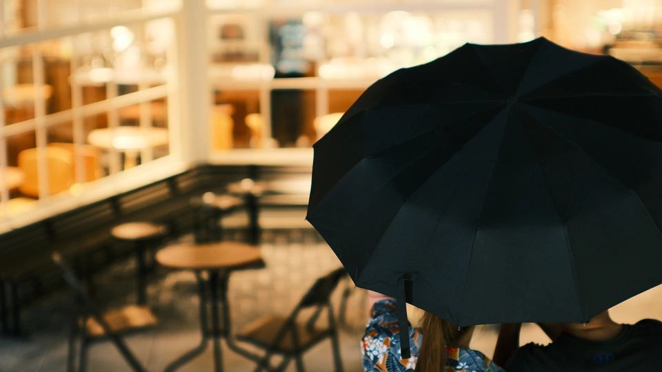 一个人坐在餐厅桌子旁 手里撑着一把打开的黑色雨伞。