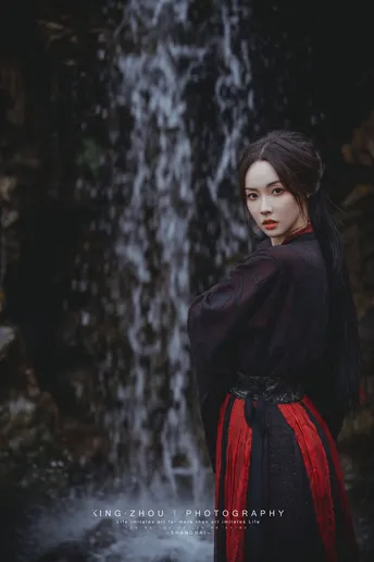 一位穿着黑色连衣裙的女士站在瀑布前