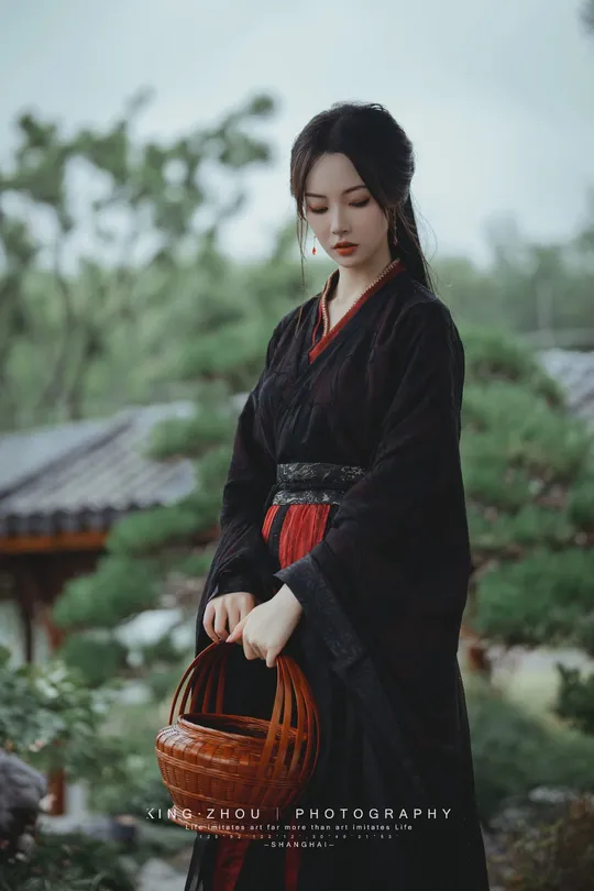 一位穿着黑色和服的女士 手提红篮 漫步在花园中。