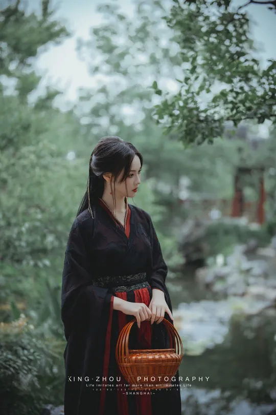 一位穿着黑色和服的女士 手提红色篮子 穿过森林 靠近河边。