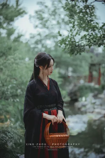 一位穿着黑色和服的女士 手提红色篮子 穿过森林 靠近河边。