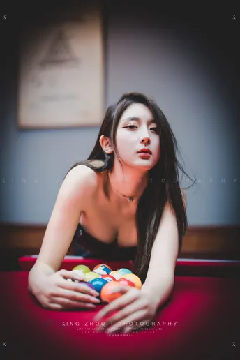 一个年轻女子坐在红色桌子旁玩台球