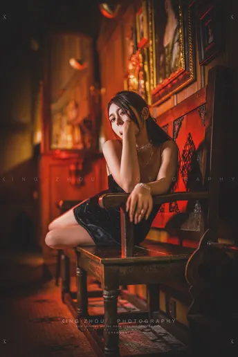 一个年轻女子坐在一个黑暗的房间里 背景有一个酒吧 木质的长凳。