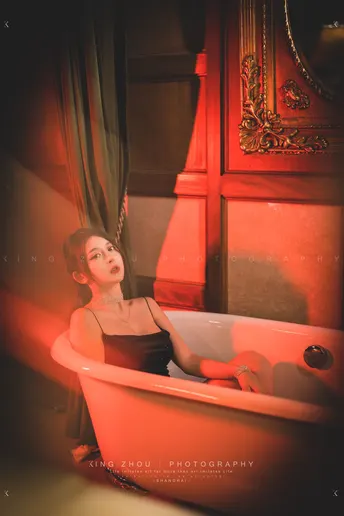 一个小女孩坐在红色的浴缸里 在浴室里 当一个年轻男孩洗澡时。