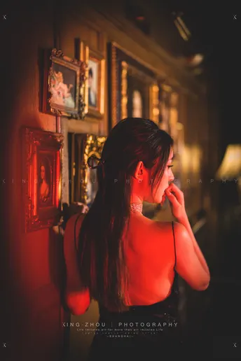 一个穿着红裙子的年轻女子站在一个由镜子照亮的黑暗房间里