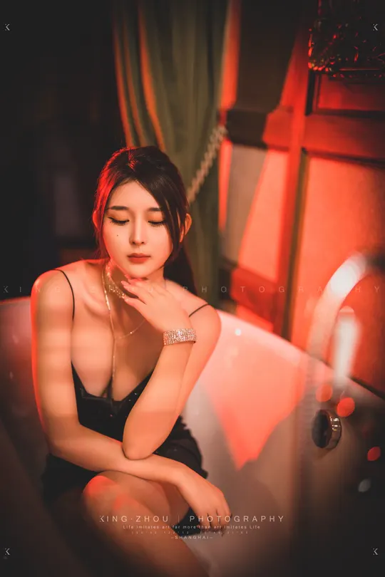 一个年轻女子坐在一个黑色椅子上 在一个光线昏暗的房间里 有一个红色的浴缸。