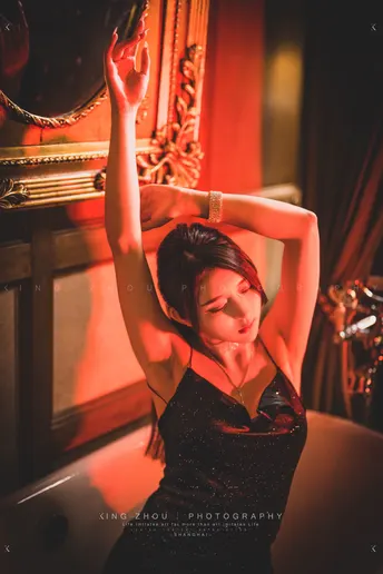 一个穿着黑色连衣裙的年轻女子在一个红色的房间里 头上顶着镜子 做出姿势。