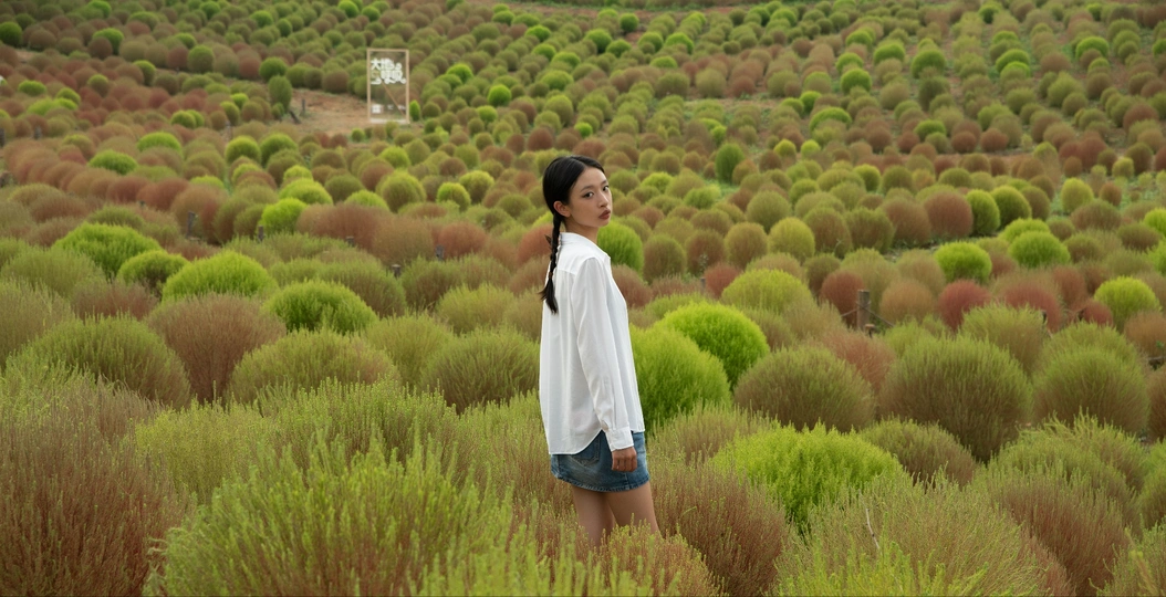 一位年轻女子站在草地上 背景中有树木。