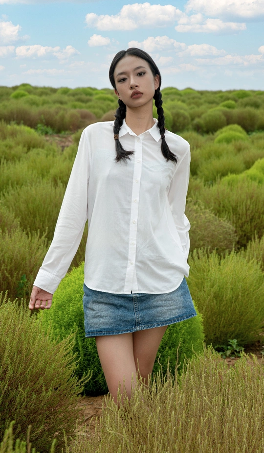 一位穿着白色衬衫的年轻女子站在一片高高的绿色草地上