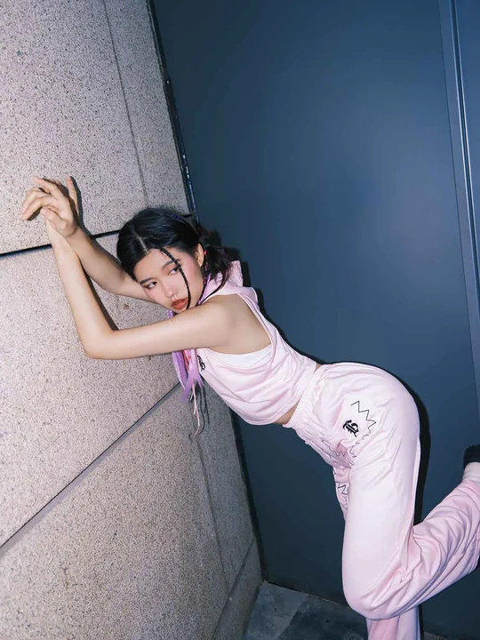 一位穿粉色裤子的年轻女子靠在一扇门旁的墙上