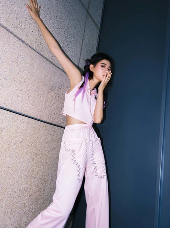 一位穿着白色睡衣的年轻女子靠在墙上 同时穿着粉色裤子 正在打电话。