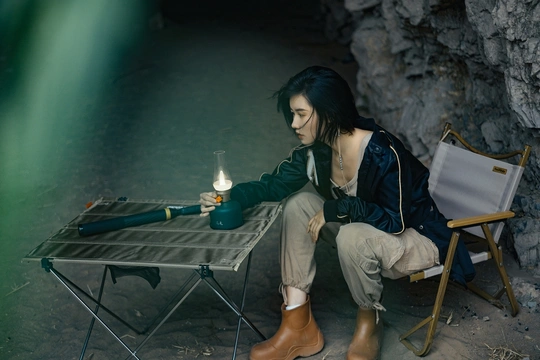 一个年轻女子坐在洞穴里 桌子上有一盏灯和茶。