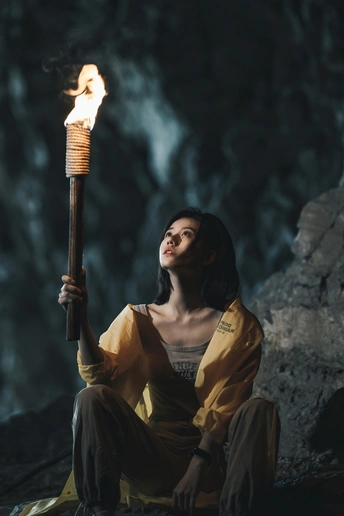 在洞穴里的一位女性 手持一根点燃火焰的魔杖 坐在地上 手中拿着一盏灯。