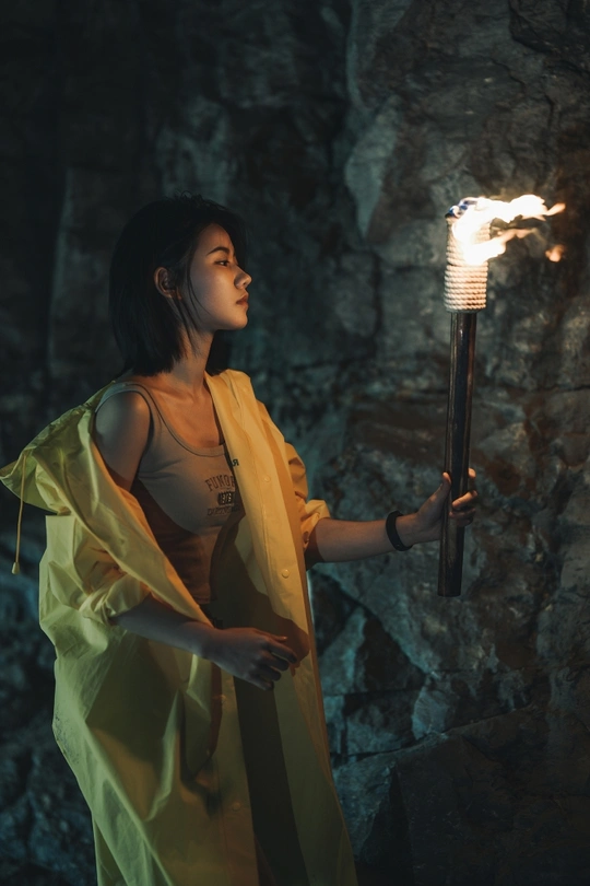 一个年轻女子在一个洞穴里拿着一个灯笼 手中有点燃的火焰 站在一个拿着点燃蜡烛的人的前面。