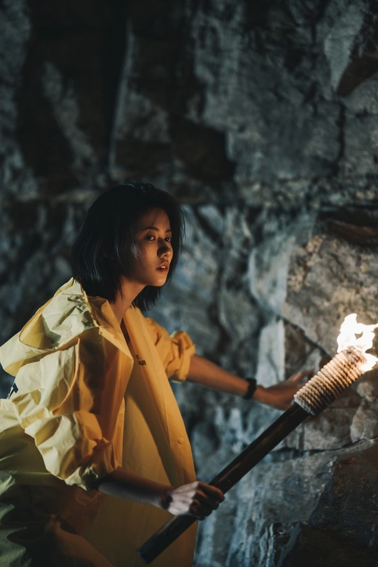 一位穿着黄色雨衣的女子手持一盏点燃的火炬在一座洞穴中。