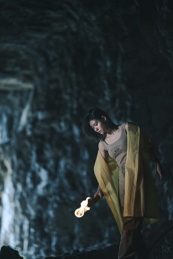 一位穿着黄色连衣裙的年轻女子穿过一个由火焰照亮的洞穴。