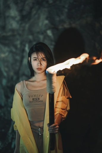 一位年轻女子手持火炬站在一个有火焰的洞穴中