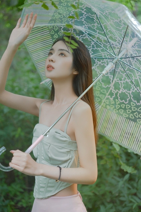 一位穿着绿色衣服的年轻女子举着一把透明的伞。