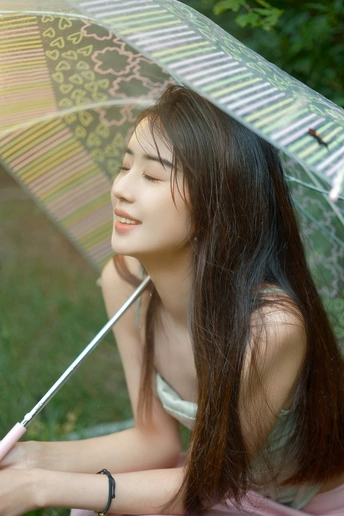 一位年轻女子手持雨伞坐在草地上