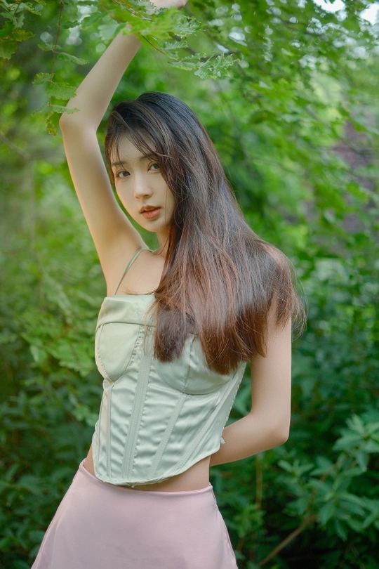 一位穿着绿色裙子的年轻女子站在森林中 举着树冠在头上。