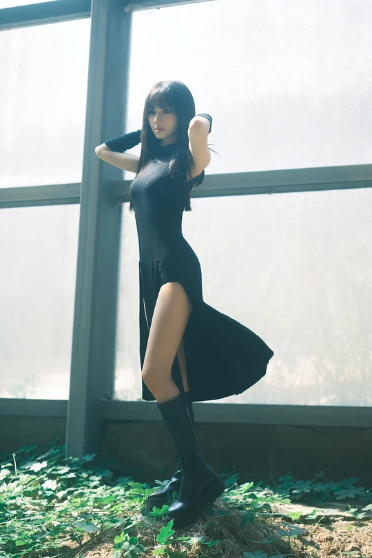 一位穿着黑色连衣裙和靴子的年轻女子站在窗户前