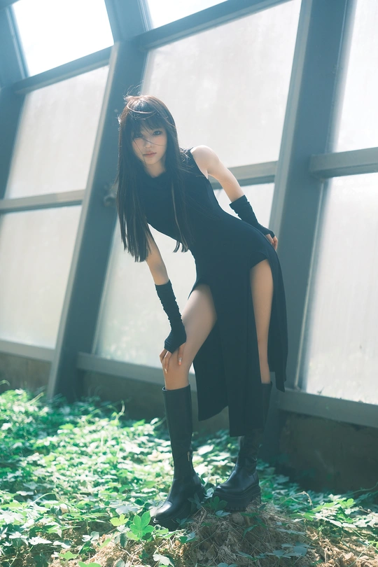 一位穿着黑色连衣裙和高筒靴的年轻女子站在窗户前