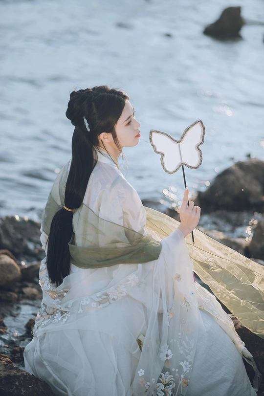 一位穿着白色连衣裙的美女手持蝴蝶在水边