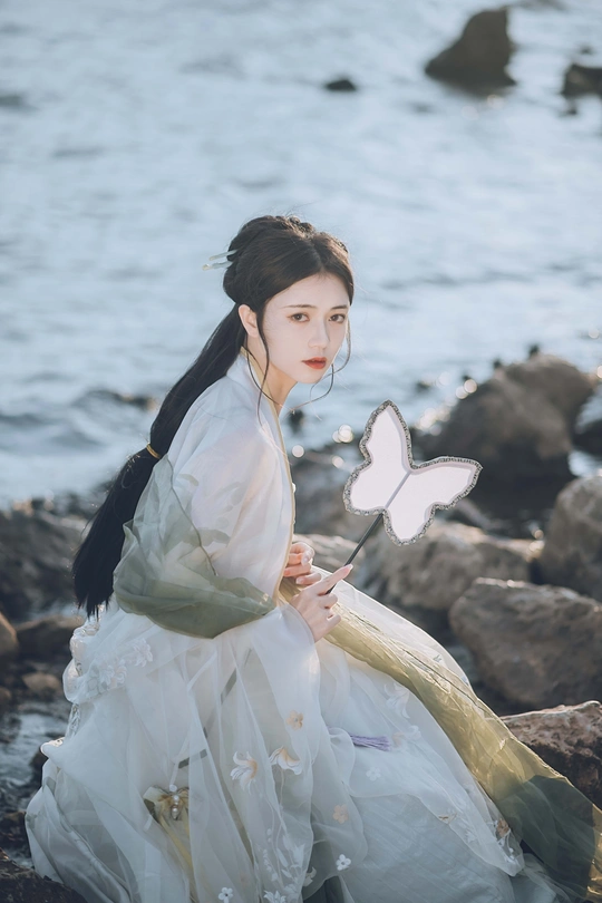 一位穿着白色连衣裙 蝴蝶停在岩石上的美女在海边