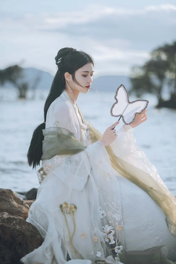 一位穿着传统裙子的美丽女孩 蝴蝶停在岩石上 岩石靠近水边。