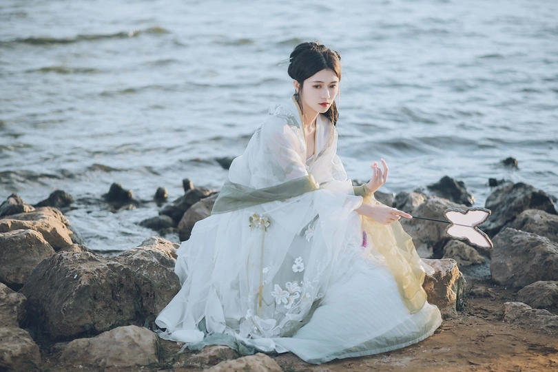 一位穿着白色服装的女子在海边的岩石上