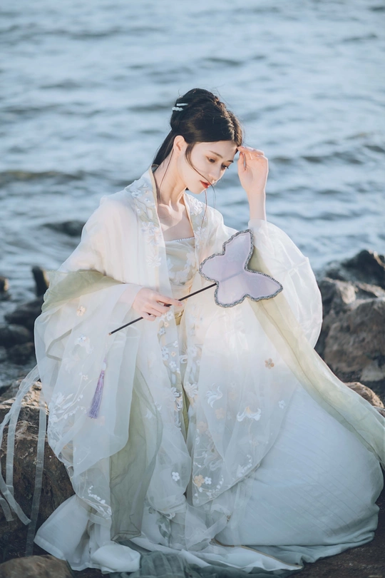 一位穿着白色传统服装的美丽女士在水边岩石上