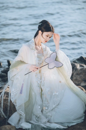 一位穿着白色传统服装的美丽女士在水边岩石上