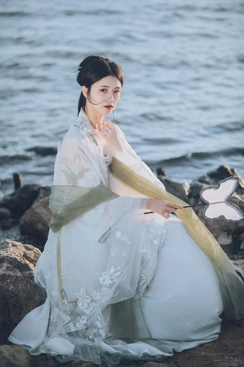 一位穿着白色长裙的美女在靠近水的岩石上。