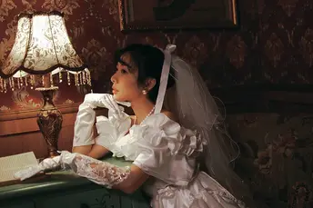 一个穿着白色连衣裙的年轻女子坐在桌子旁 正在阅读一本书 桌子上有一盏灯。