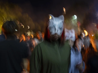 一群人在夜晚沿着街道行走 其中一个人脸上戴着面具。